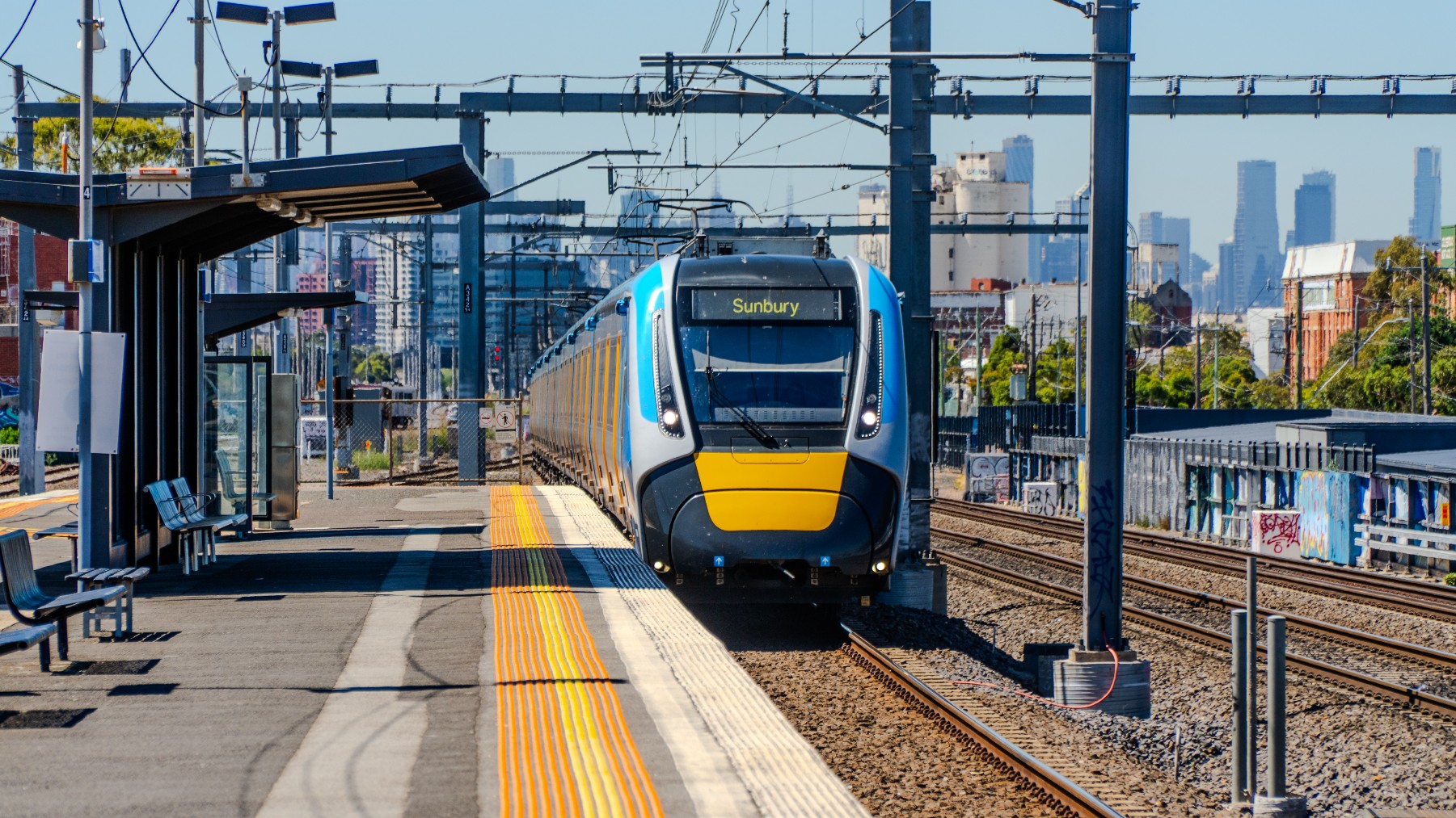 A Melbourne train approaching a station on the Sunbury line with the city skyline in the background, on a corridor set for major upgrades under Melbourne Airport Rail