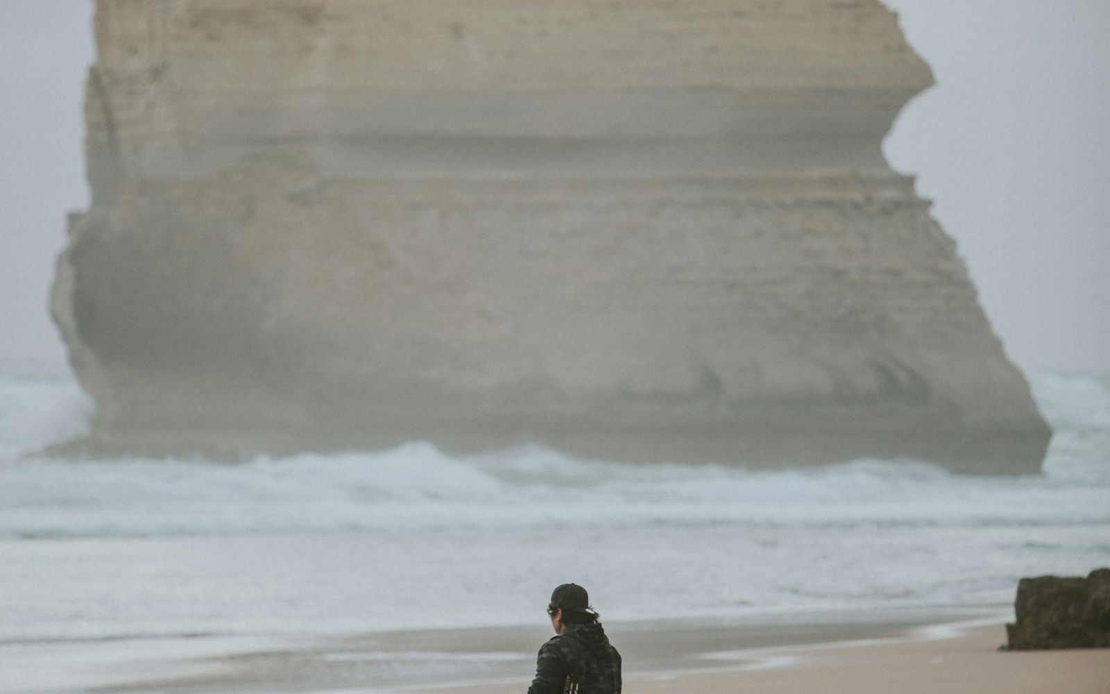 A visitor stands on the beach below one of the Twelve Apostles limestone stacks at Port Campbell National Park, Victoria