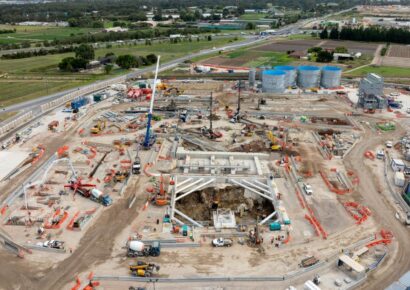 Aerial view of the Suburban Rail Loop tunnel boring machine launch site in Clarinda, showing large-scale construction activity, slurry separation silos and heavy machinery across the site with Melbourne's southeast suburbs in the background.
