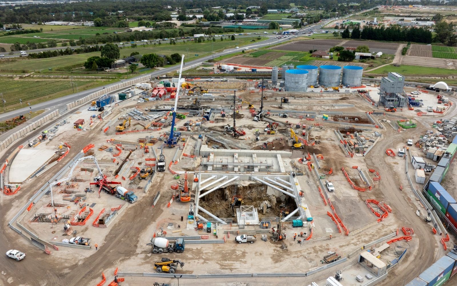 Aerial view of the Suburban Rail Loop tunnel boring machine launch site in Clarinda, showing large-scale construction activity, slurry separation silos and heavy machinery across the site with Melbourne's southeast suburbs in the background.