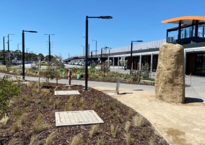 Alt text: The landscaped forecourt at Deer Park Melbourne train station, showing native plantings, young trees and one of three giant boulders oriented toward nearby mountain ranges