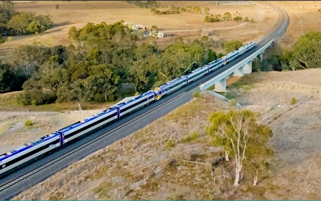 Alt text: Two V/Line VLocity trains crossing a rail bridge through open farmland on Melbourne's western corridor.