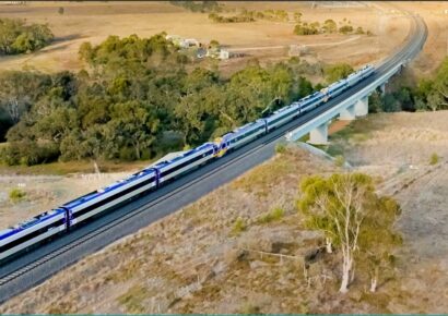 Alt text: Two V/Line VLocity trains crossing a rail bridge through open farmland on Melbourne's western corridor.