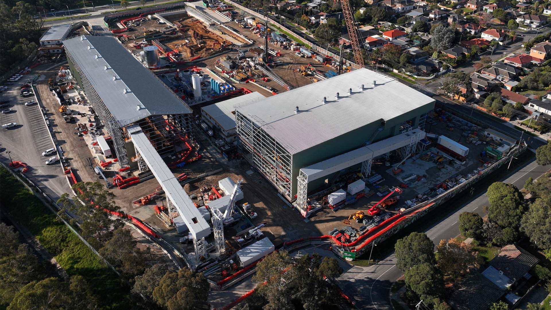 Aerial view of a Suburban Rail Loop East tunnel boring machine launch site, with acoustic sheds, a crane and piling rigs ringed by Melbourne housing.