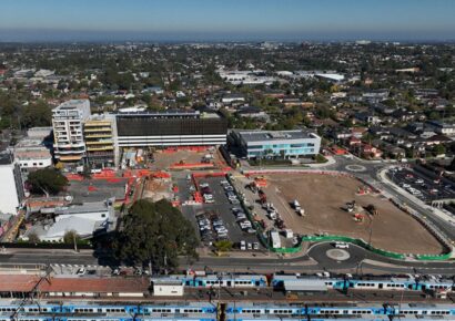 Alt text: Aerial view of a Suburban Rail Loop East station precinct beside an existing Melbourne train line, with car parks and a cleared construction site.