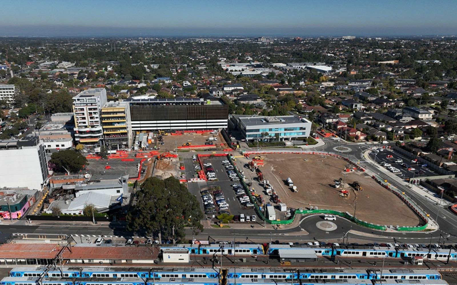 Alt text: Aerial view of a Suburban Rail Loop East station precinct beside an existing Melbourne train line, with car parks and a cleared construction site.