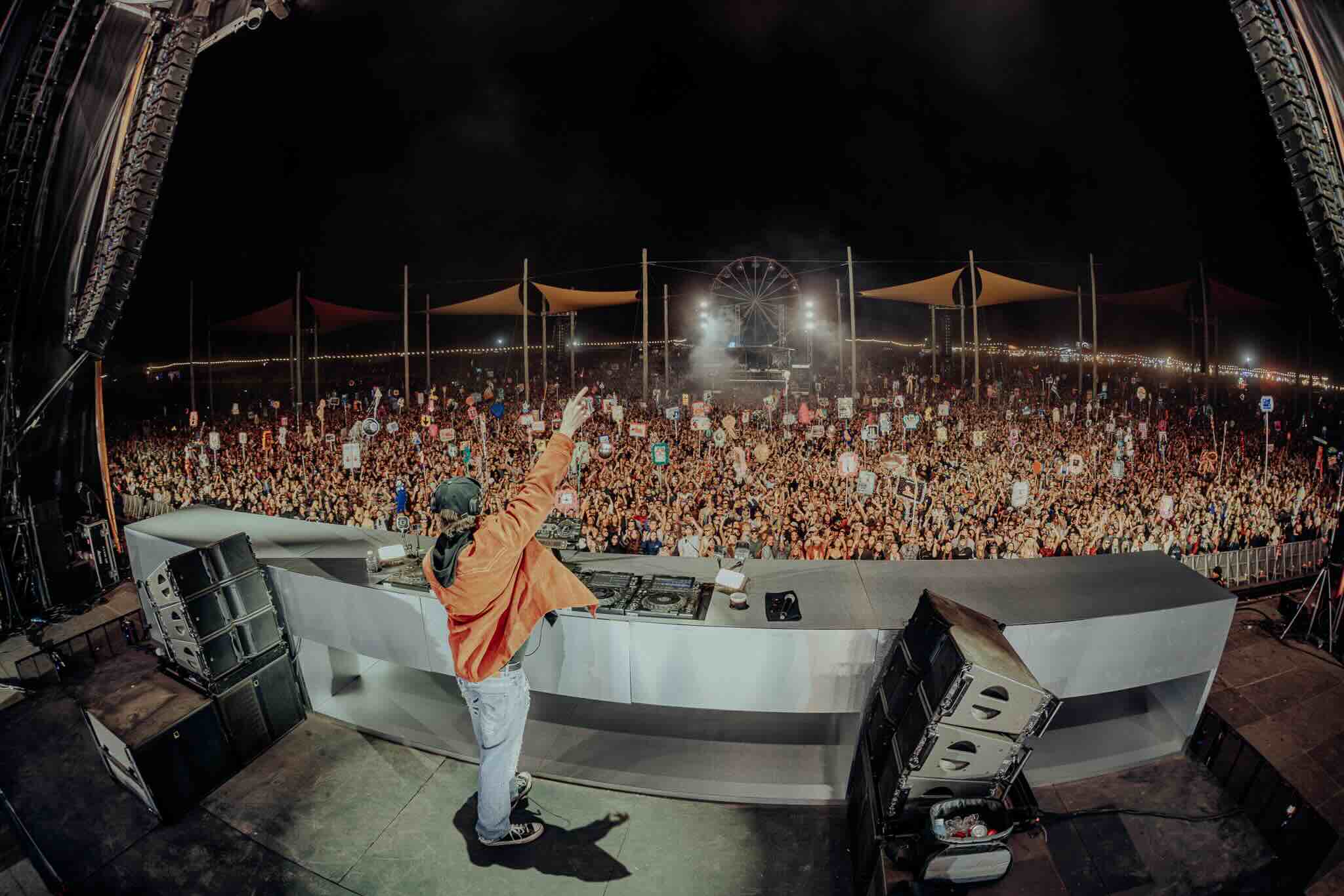 A DJ raises an arm to a huge night crowd under a Ferris wheel at Beyond The Valley, where the 2026 BTV lineup lands this New Year's.