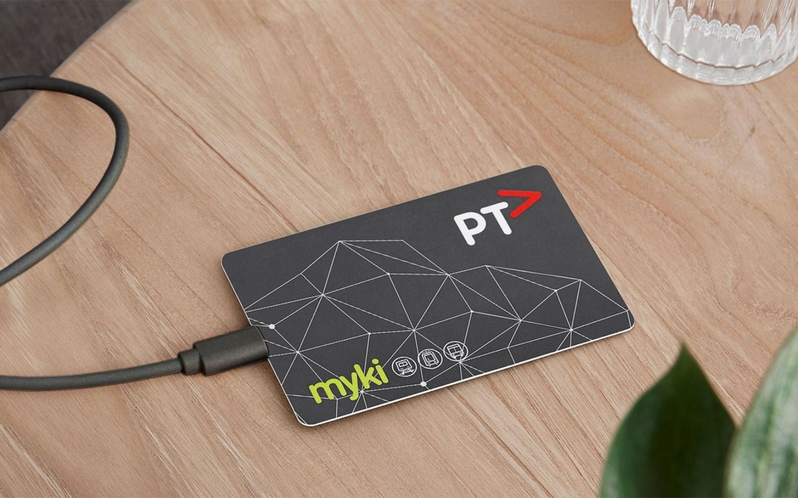 Alt text: A myki card resting on a wooden table with a charging cable beside it, showing the myki and PTV logos.