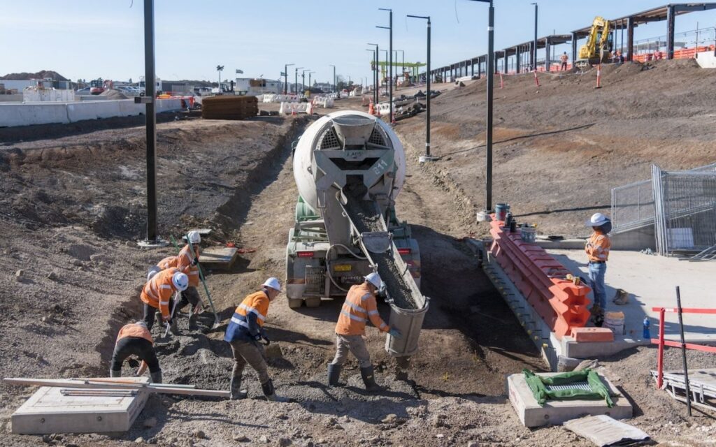 Crews pouring concrete beside new light poles at the West Tarneit construction site for the new Melbourne train station.