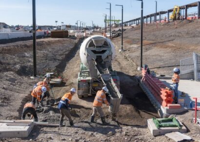 Crews pouring concrete beside new light poles at the West Tarneit construction site for the new Melbourne train station.