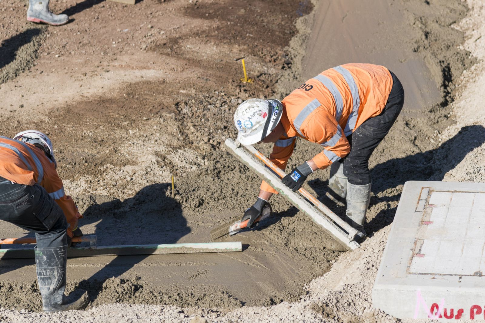 Two construction workers screed wet concrete by hand at the new Melbourne train station site at West Tarneit.