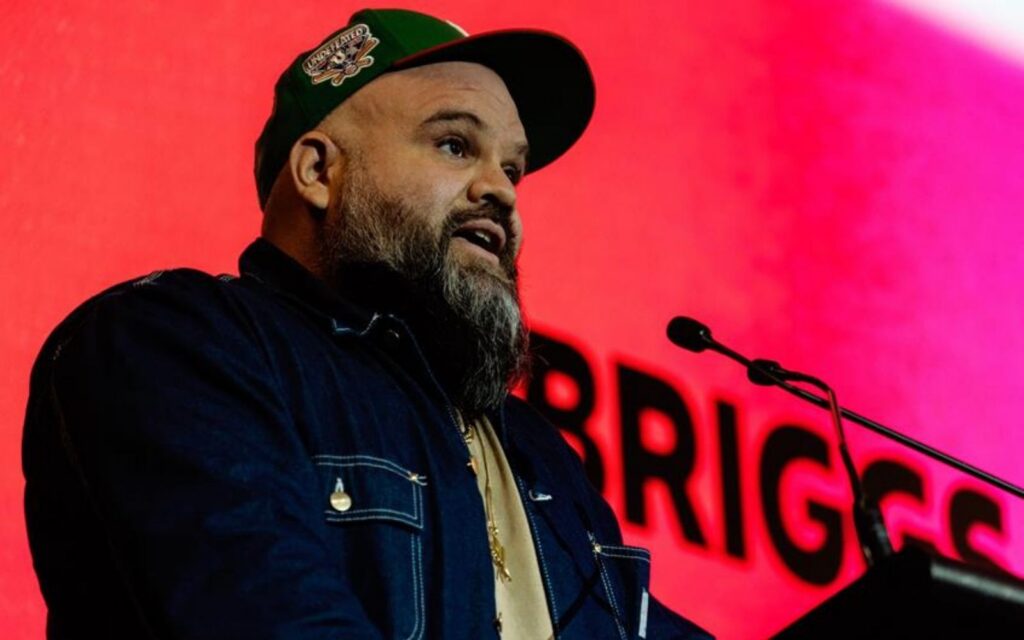 Briggs in front of a pink background, campaigning for greater music funding this Victorian election.